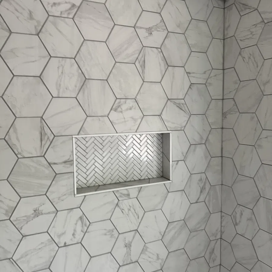 Bathroom wall with large hexagonal marble tiles and inset shelf with herringbone pattern tiles.