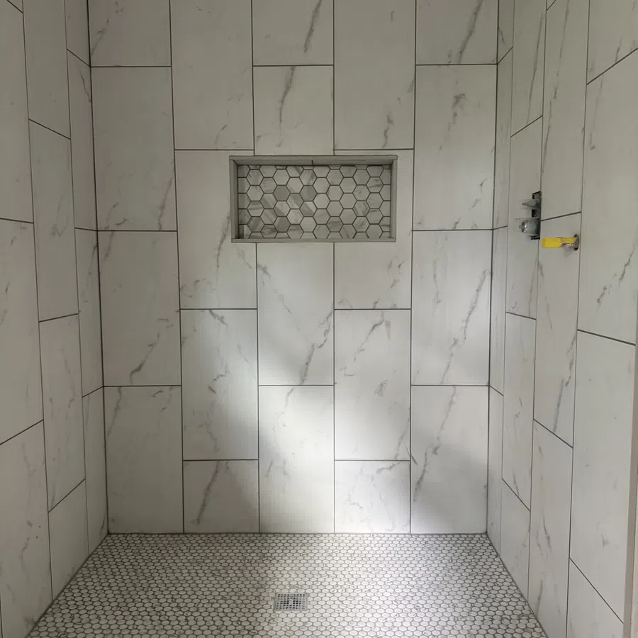Shower area with large white marble tiles on walls and small hexagonal tiles on floor featuring a built-in niche.