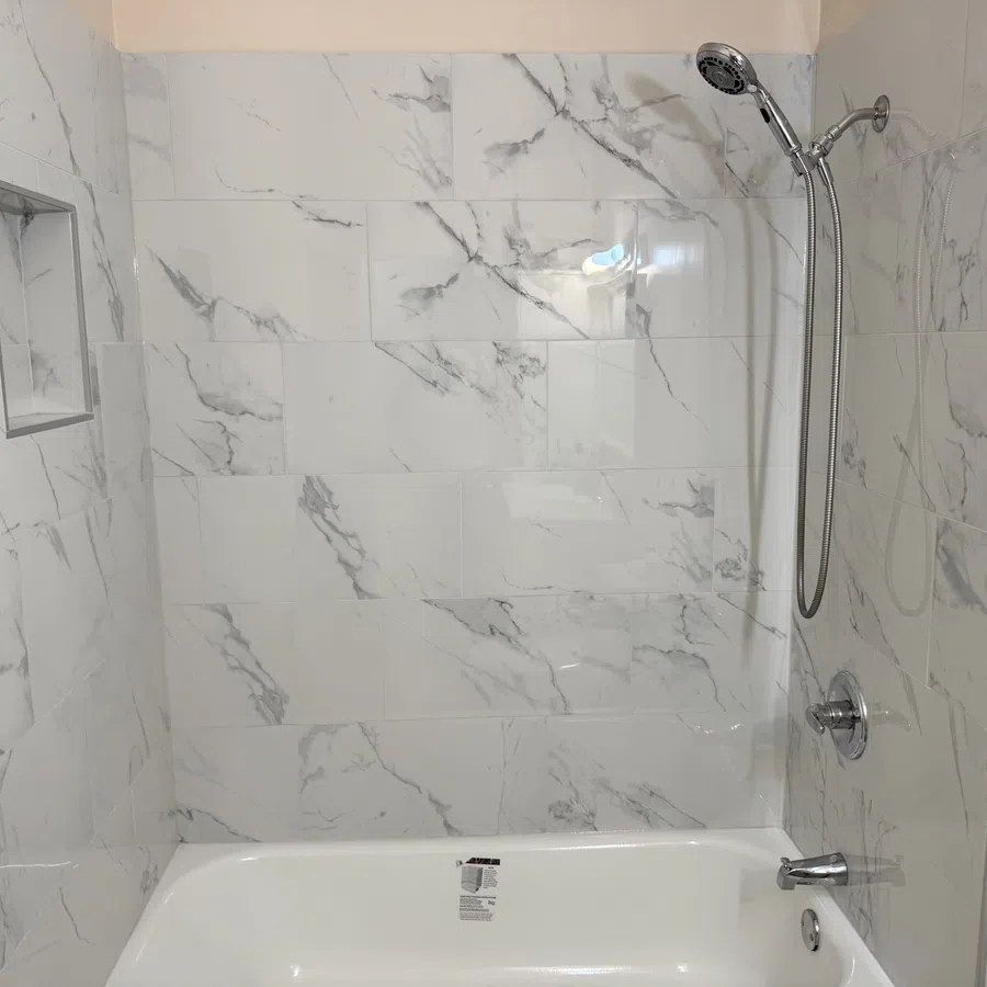 Modern bathroom with white marble tiled walls, a built-in shower niche, a bathtub, and a chrome showerhead.