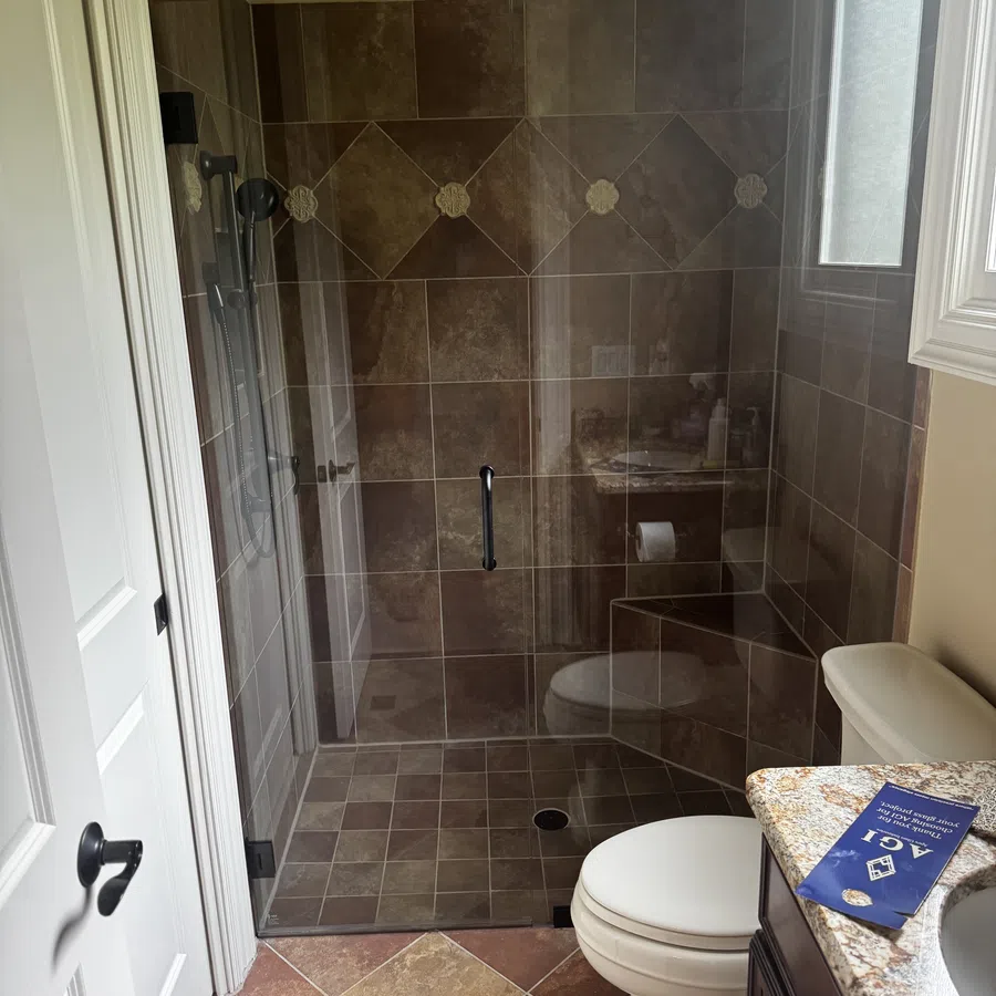 Compact bathroom with brown tile shower, glass door, white toilet, and granite countertop with brochure.