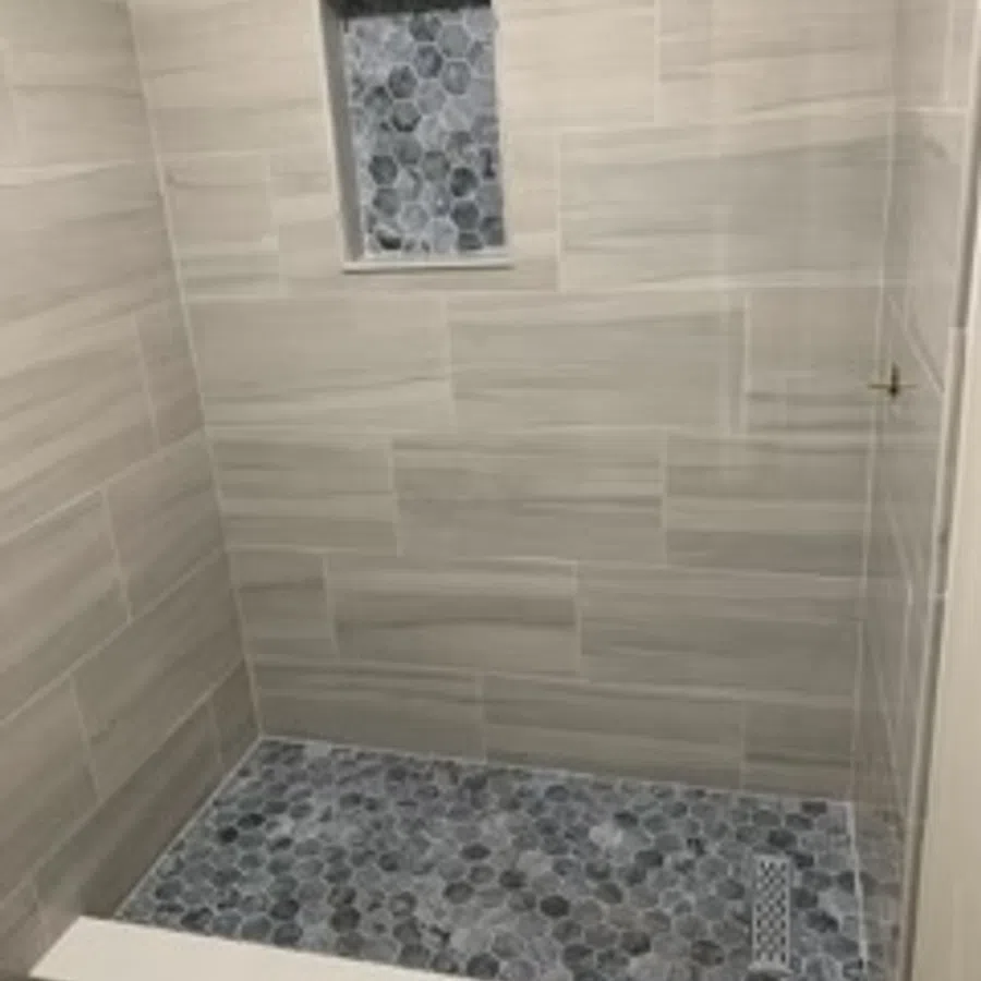 Shower with beige rectangular wall tiles and dark hexagonal mosaic floor tiles with matching niche