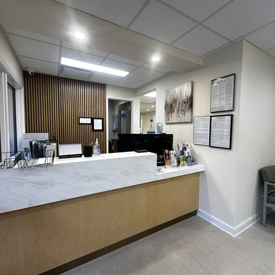 Modern medical office reception area with marble counter, wood panel accent wall, and informational brochures.