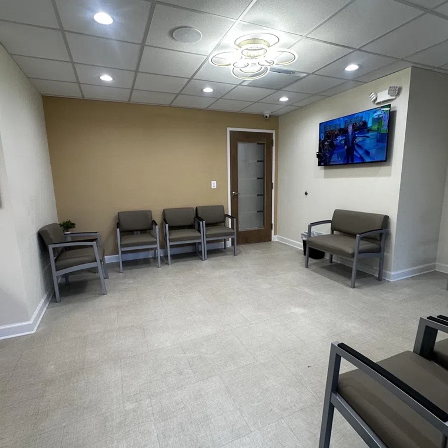 Modern medical office waiting room with chairs, wall-mounted TV, beige walls, and bright ceiling lights.