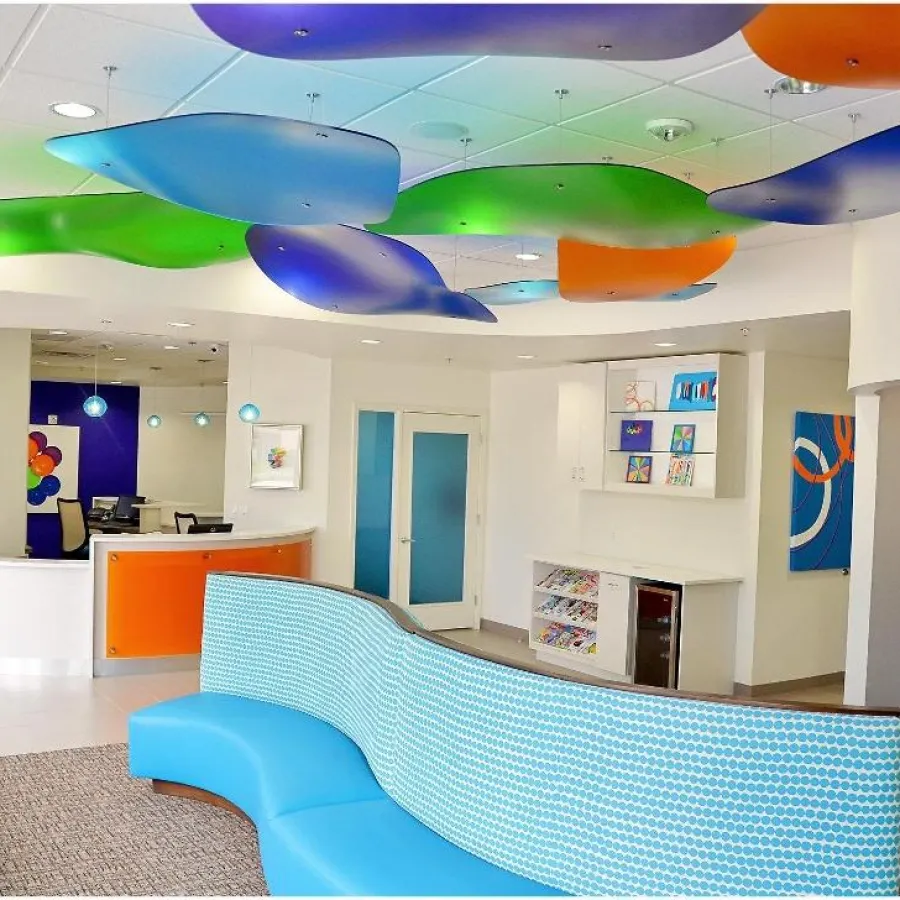 Modern waiting room with curved blue seating, colorful ceiling panels, and bright orange reception desk in clean space.