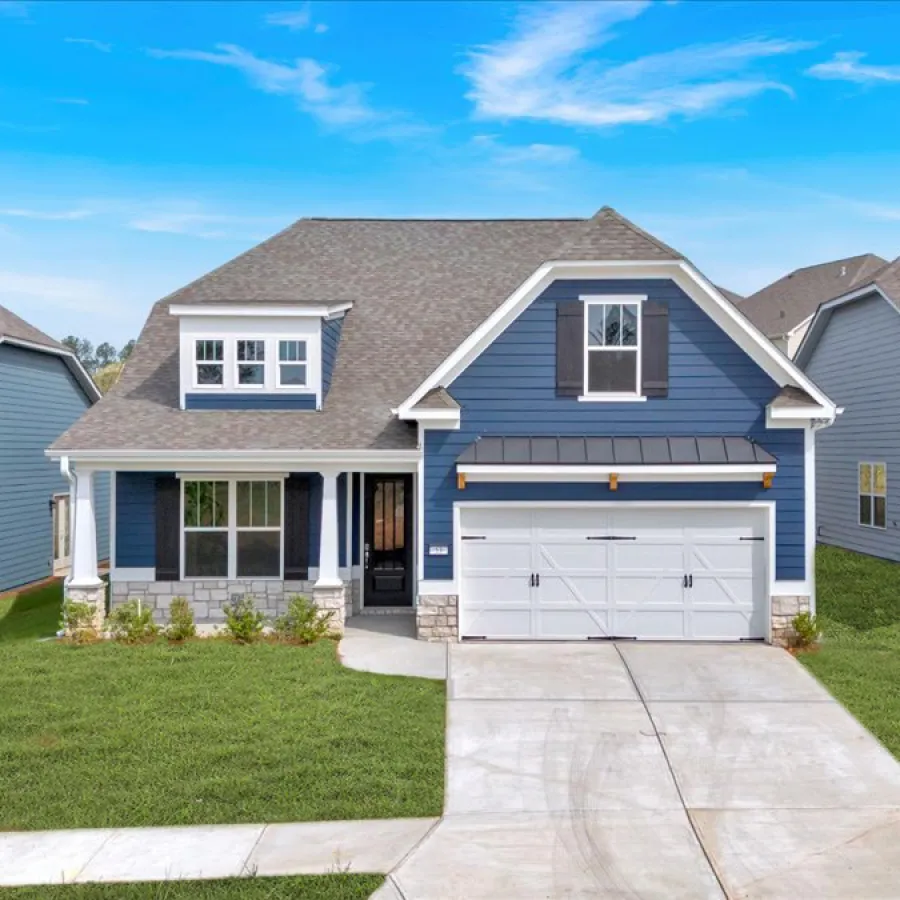 Blue two-story suburban house with white trim, attached garage, manicured lawn, and clear blue sky.