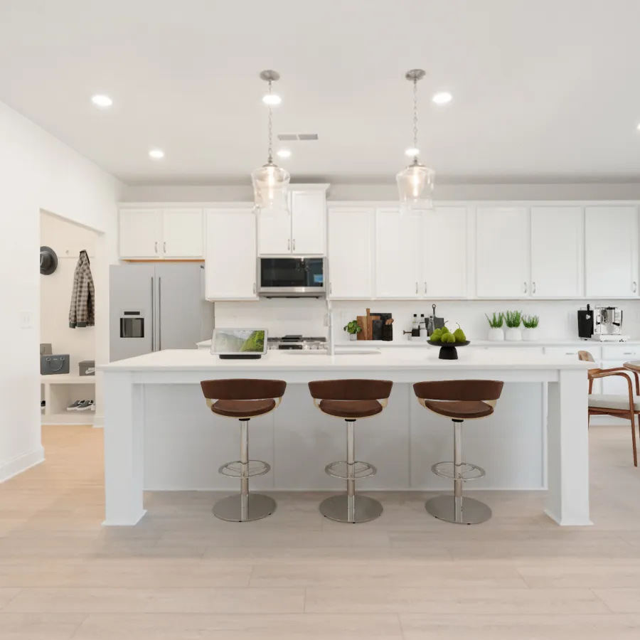 Modern white kitchen with large island, three brown bar stools, pendant lights, and wooden dining set by window.