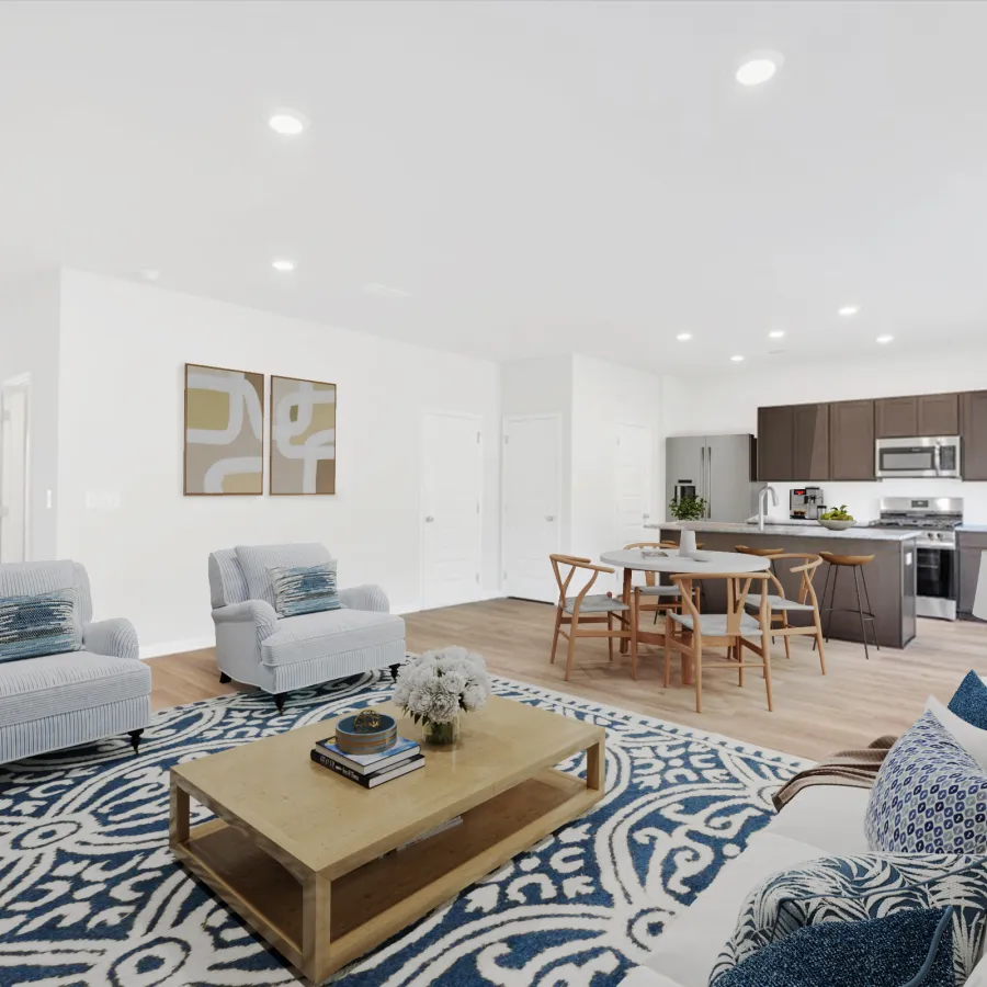 Bright open living room with blue patterned rug, white sofa, armchairs, wooden coffee table, and modern kitchen in background
