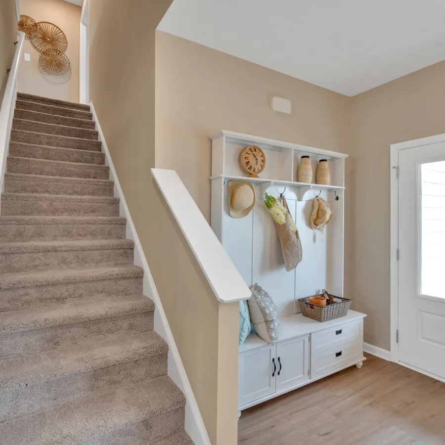 Welcoming entryway with stairs, coat rack, and decor in a light beige and white color palette.
