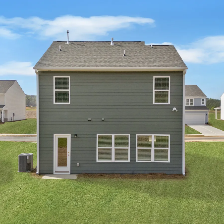 Back view of a modern green house with a yard and neighboring homes under a clear blue sky.