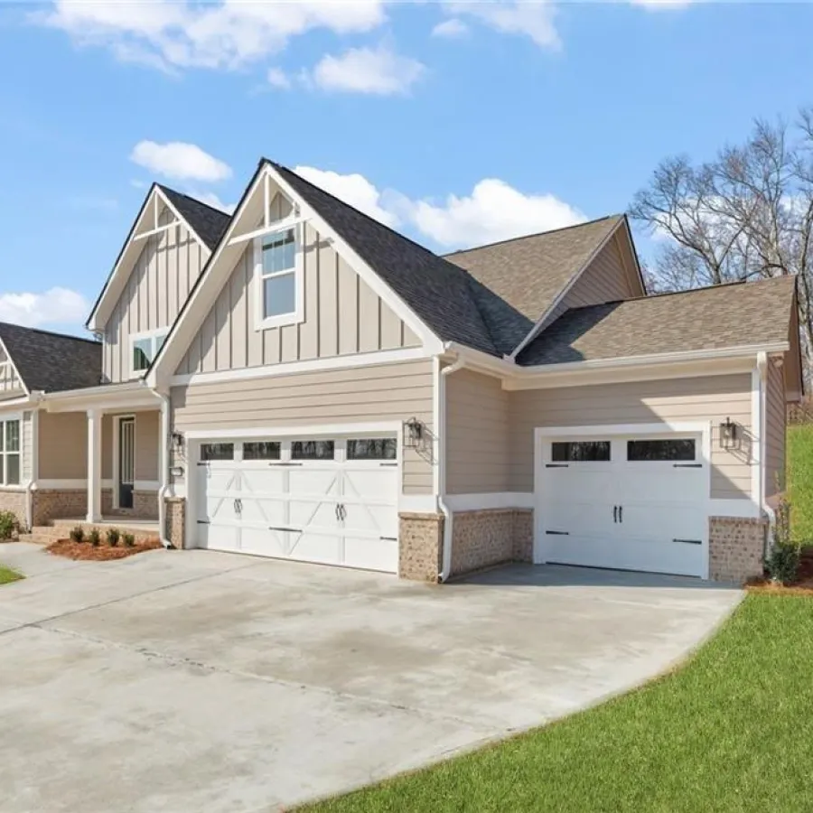 Modern beige house with white garage doors, concrete driveway, and grassy yard under a blue sky