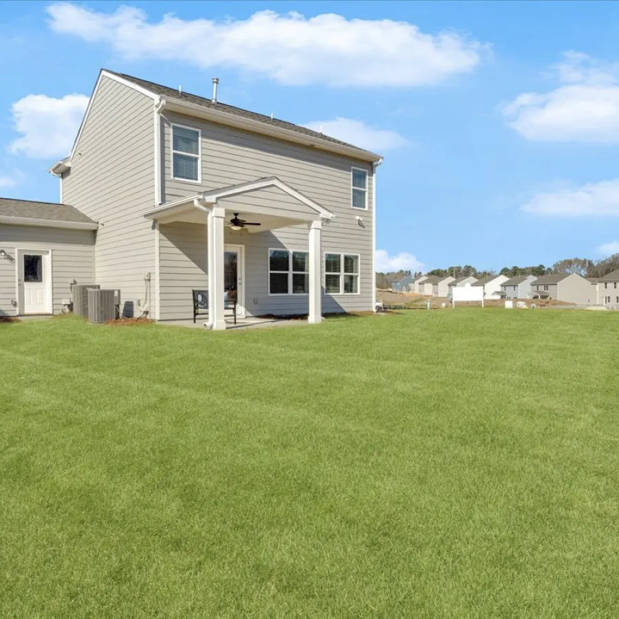 Charming two-story house with a spacious green lawn under a blue sky.
