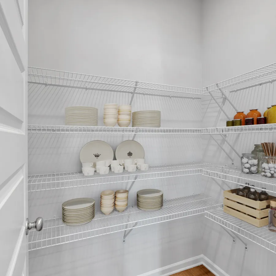 Organized pantry with white wire shelves holding dishes, jars, bottles, and a wooden crate in a bright white room.