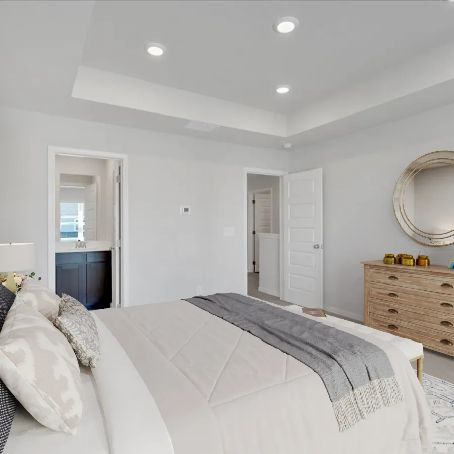 Bright modern bedroom featuring a large bed, soft gray bedding, wooden dresser, and round mirror on white walls.