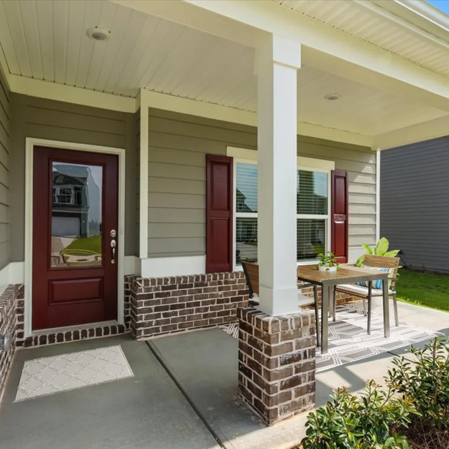 Covered front porch with brick pillars, gray siding, maroon door, outdoor table and chairs on concrete floor.