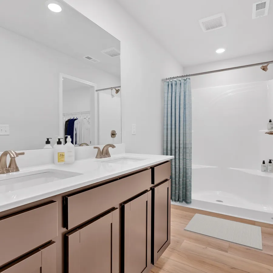 Bright modern bathroom with double sinks, a spacious shower, and light wood flooring.