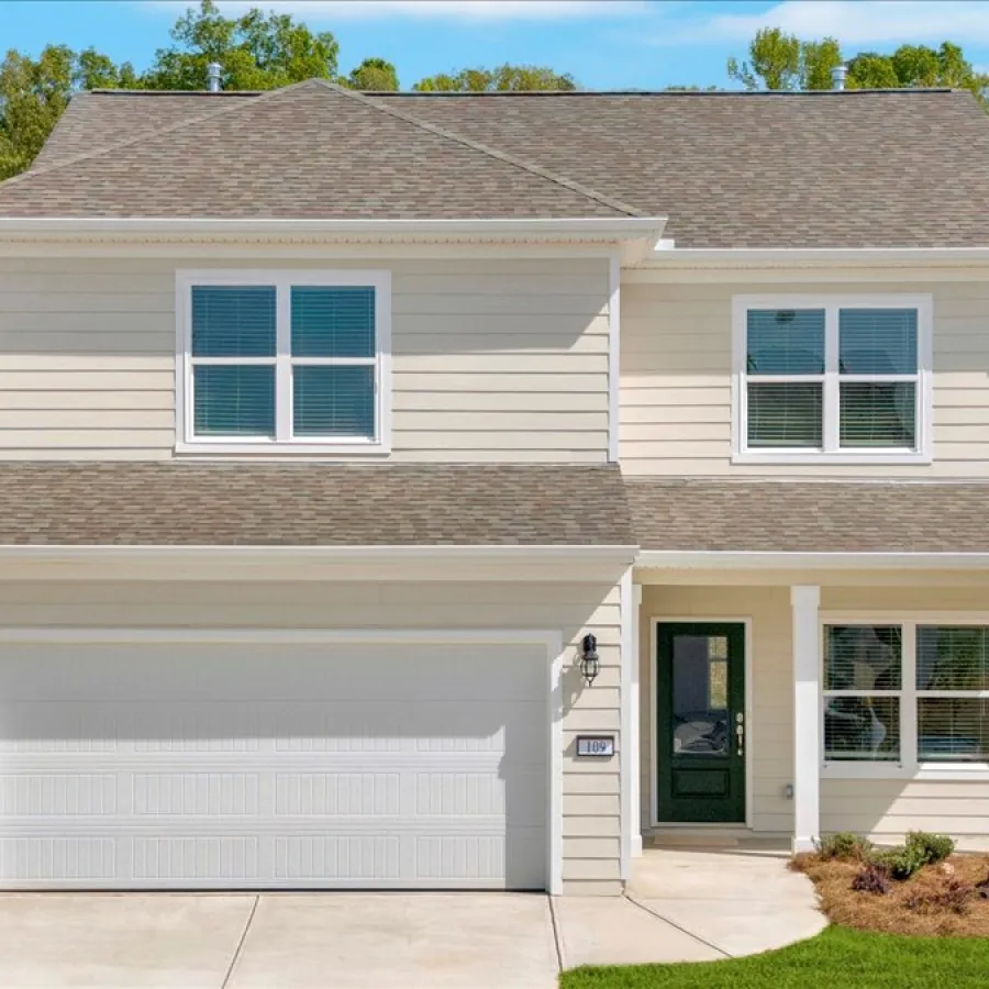 Modern two-story beige house with attached garage, green front door, and landscaped lawn under a clear sky.