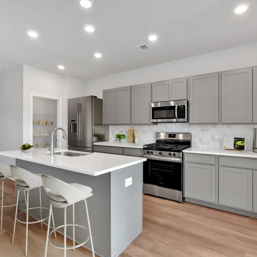 Modern kitchen with gray cabinets, white countertops, stainless steel appliances, and a kitchen island with bar stools.