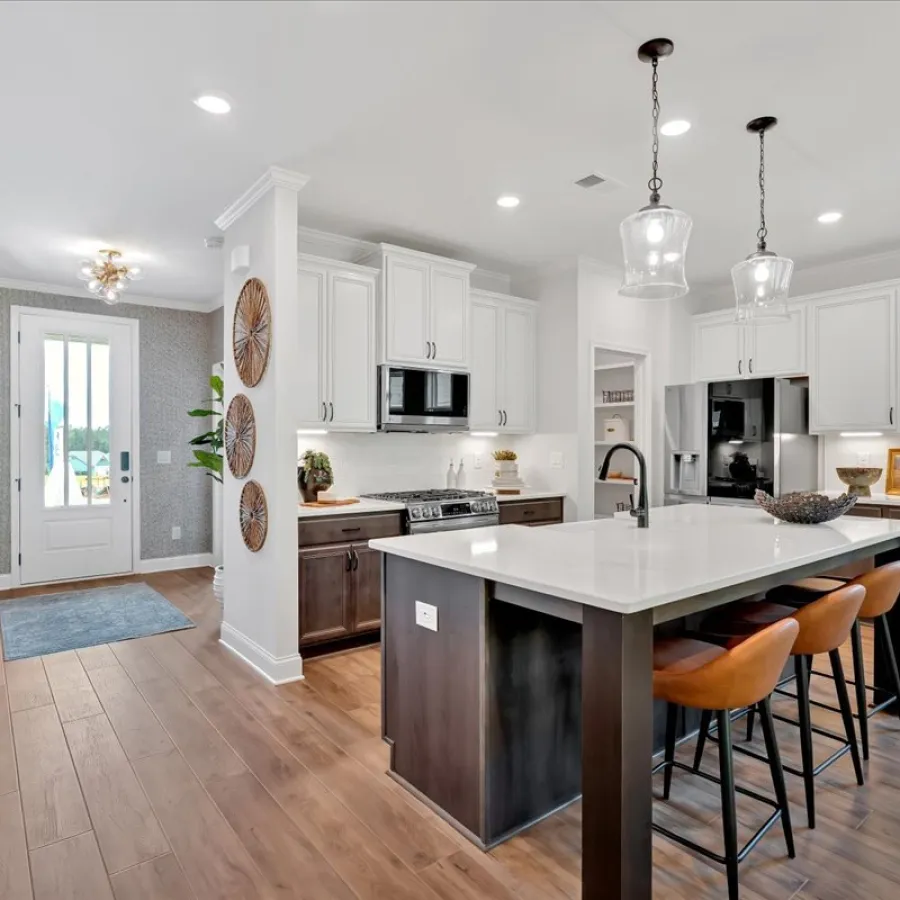 Modern kitchen with white cabinets, large island, pendant lights, wood flooring, and green accent wall