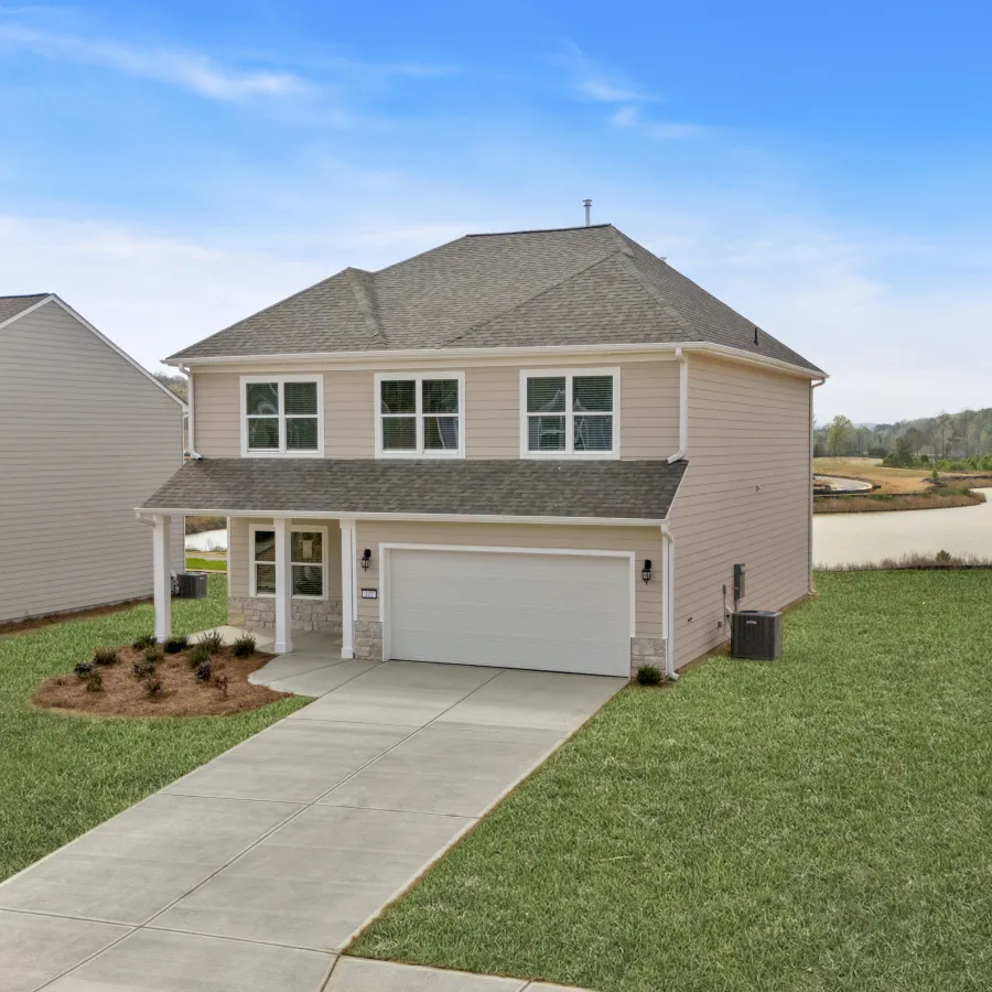 Modern two-story house with beige siding, a two-car garage, and spacious front lawn under a blue sky.