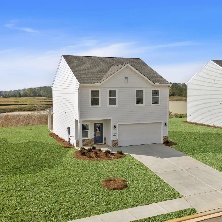 New suburban two-story white house with attached garage and neatly landscaped green lawn under blue sky.