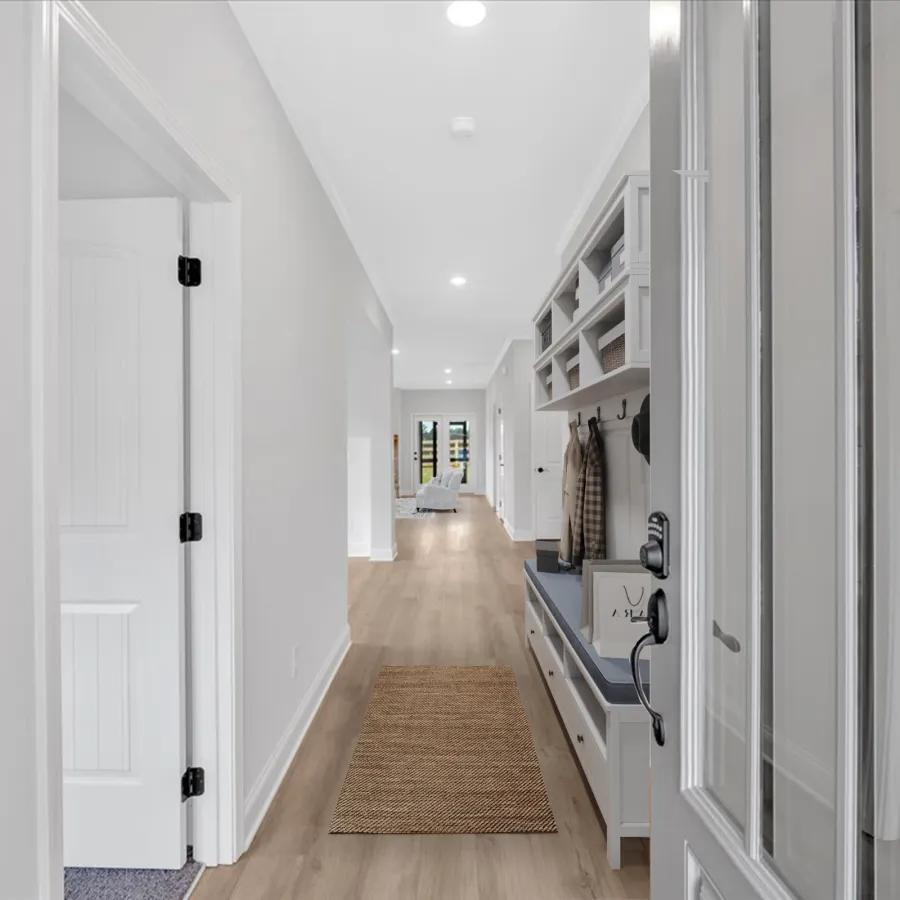 Bright modern hallway with light wood floors, white walls, built-in bench, hooks, and recessed lighting.