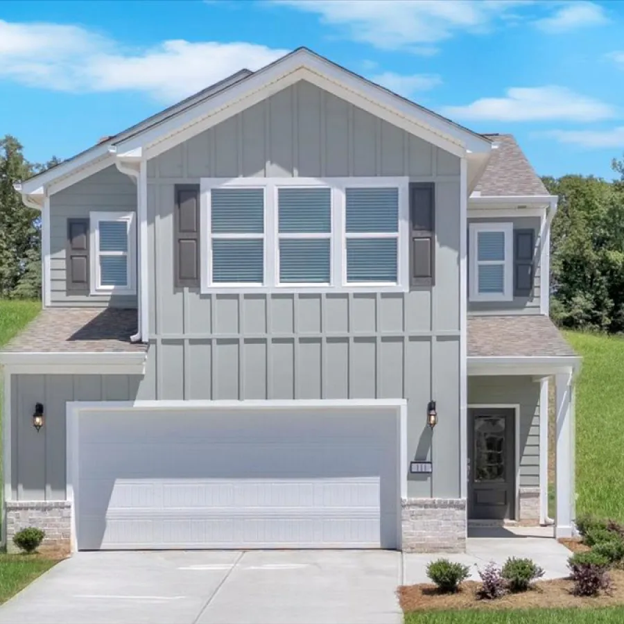 Modern two-story gray house with white garage door, dormer windows, and green lawn under a blue sky.
