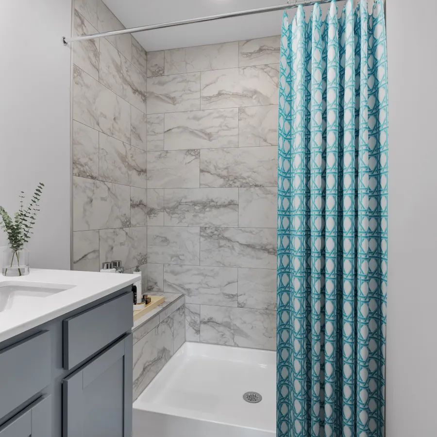 Modern bathroom with marble tiled shower, white countertop vanity, blue cabinetry, and patterned blue shower curtain