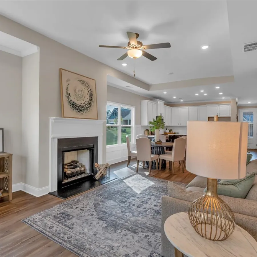 Bright open living room with fireplace, ceiling fan, dining area, modern decor, and hardwood floors
