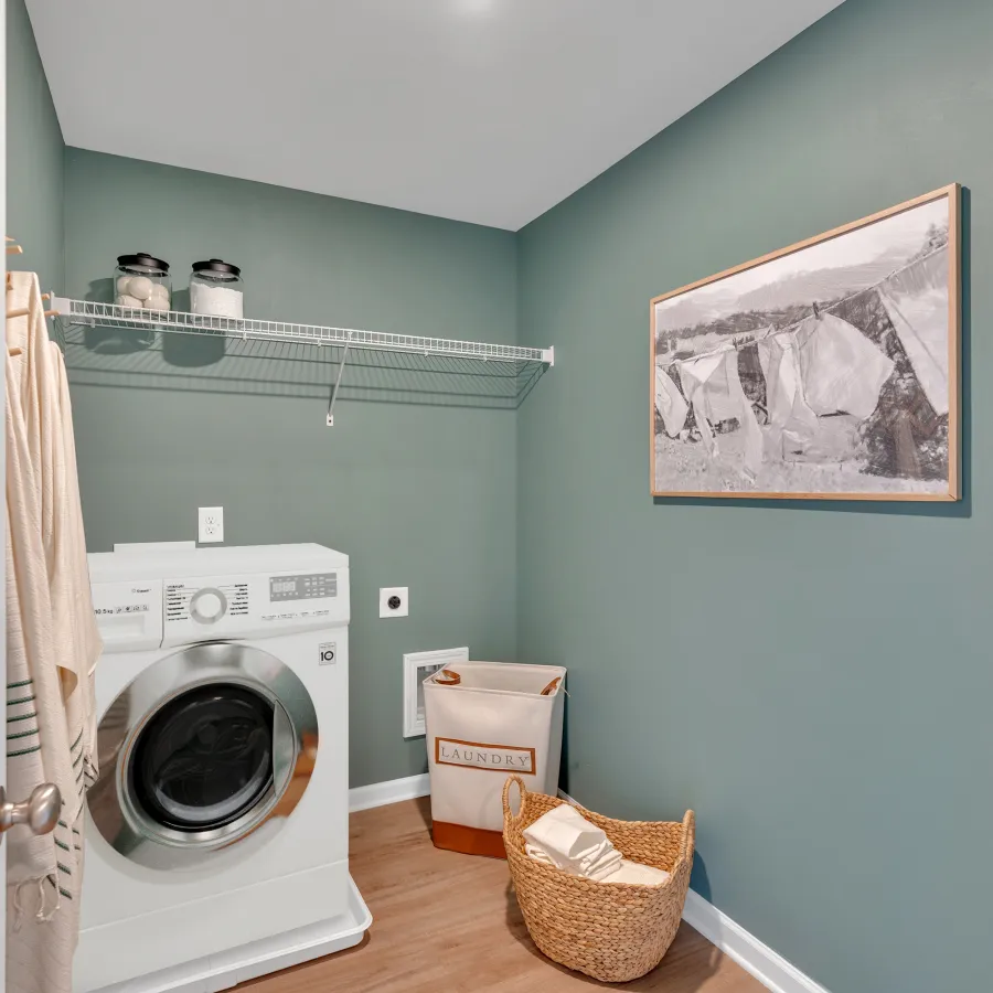 Bright laundry room featuring a washing machine, shelves, and decorative wall art.