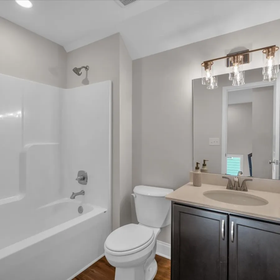 Modern bathroom with white bathtub, toilet, dark wood vanity, beige countertop, and decorative light fixture