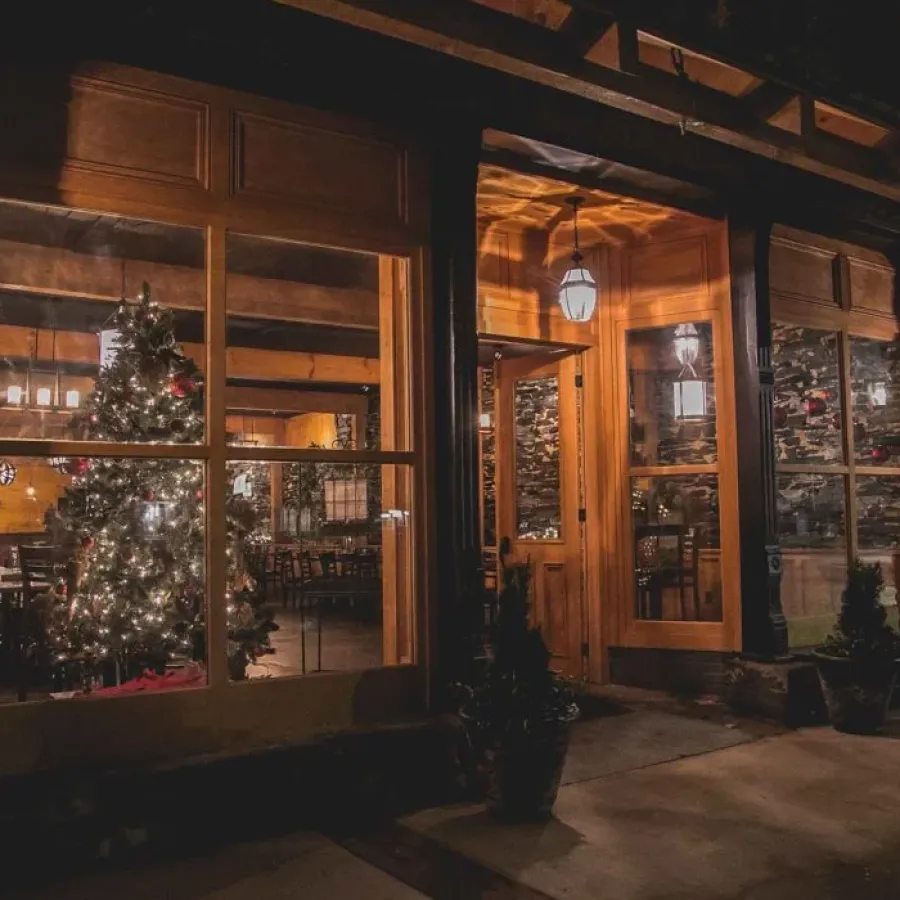 Cozy warmly lit restaurant entrance with decorated Christmas tree visible through large windows at night.