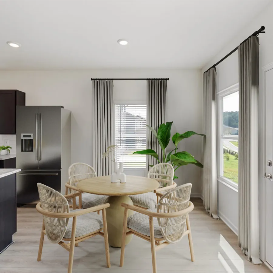 Bright dining area with round wooden table, four wicker chairs, large windows, and modern kitchen in the background.