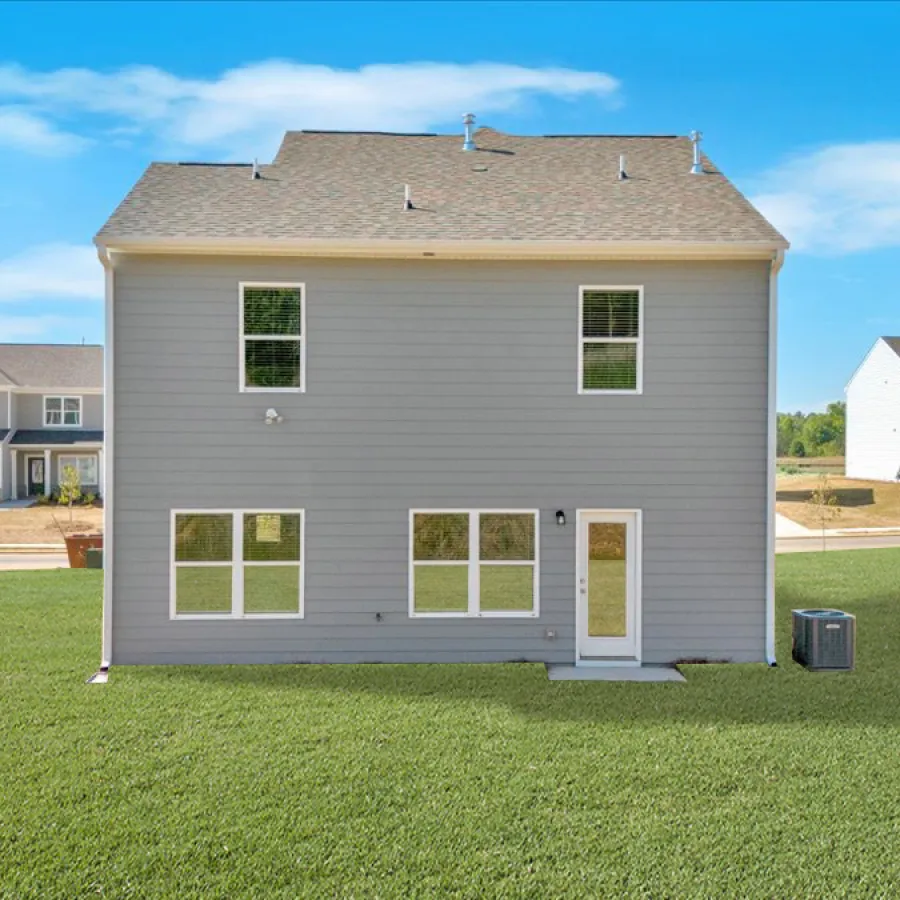 Back view of a two-story gray house with large yard, surrounded by similar suburban homes under a blue sky