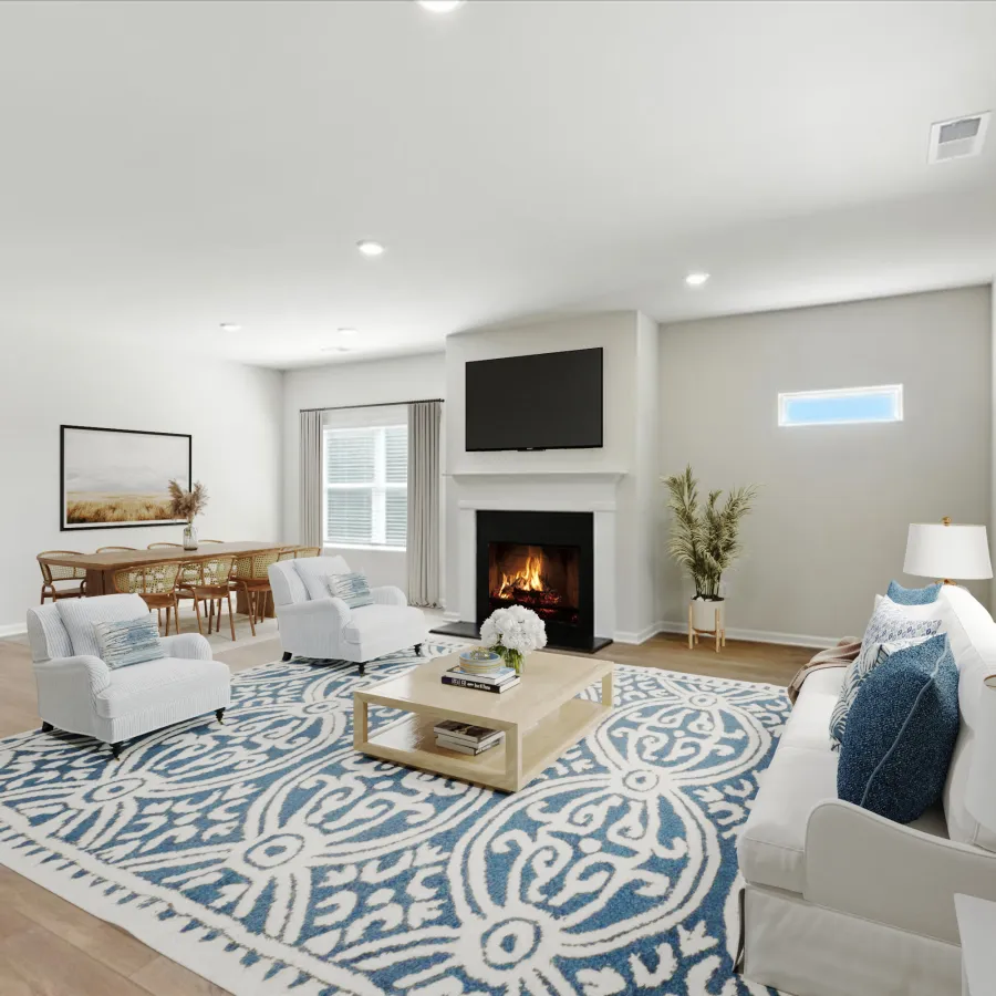 Bright modern living room with white furniture, blue patterned rug, fireplace, large windows, and wooden dining table.