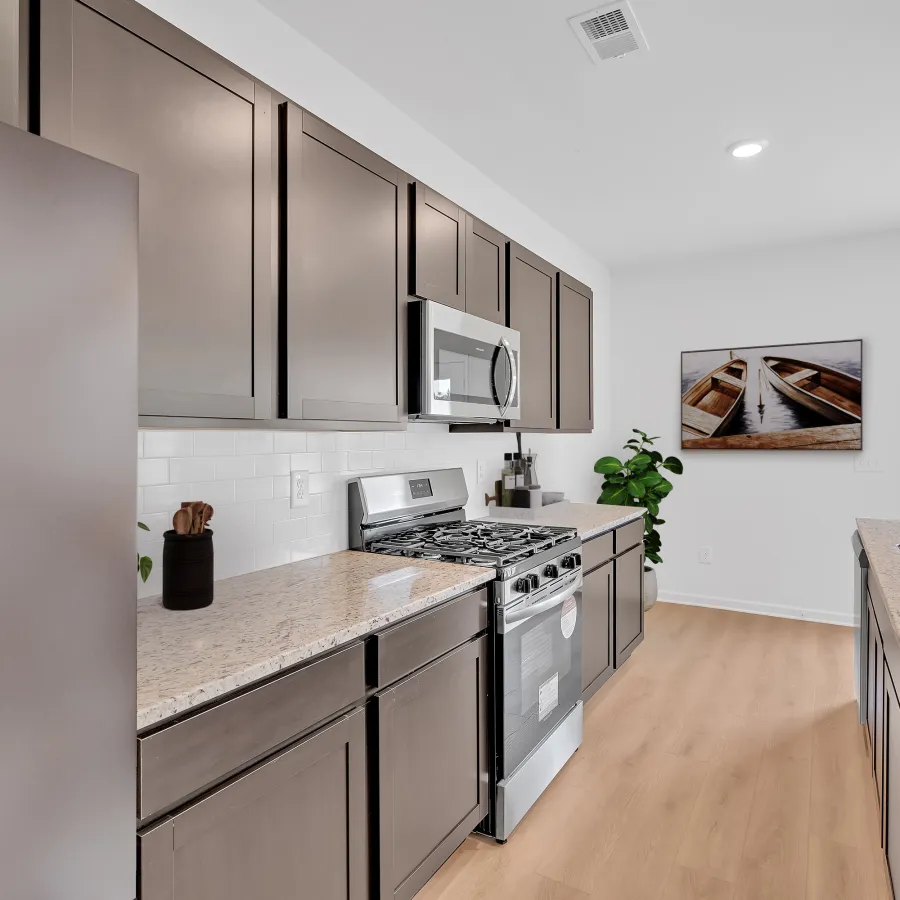 Modern kitchen with stainless steel appliances, dark cabinets, light granite countertops, and wood flooring.