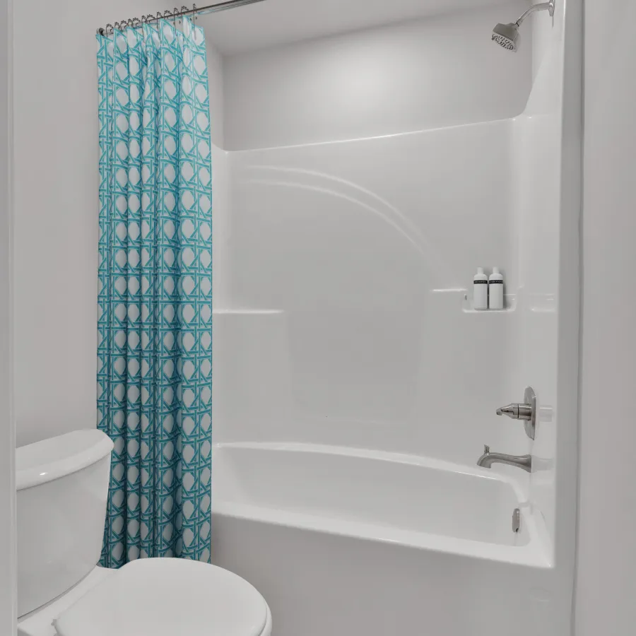 Small clean white bathroom with bathtub, blue patterned shower curtain, and toilet on wood floor