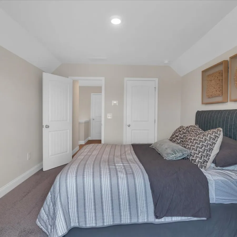 Minimalist bedroom with gray striped bedding, upholstered headboard, decorative wall art, and neutral walls.