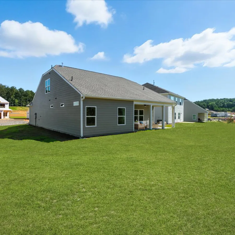 Modern suburban house with large green lawn under blue sky and scattered clouds on a sunny day.