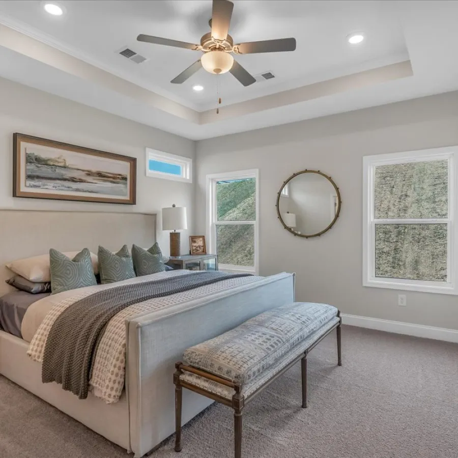 Modern bedroom with plush bed, patterned bench, ceiling fan, two windows, and minimalistic decor in soft tones