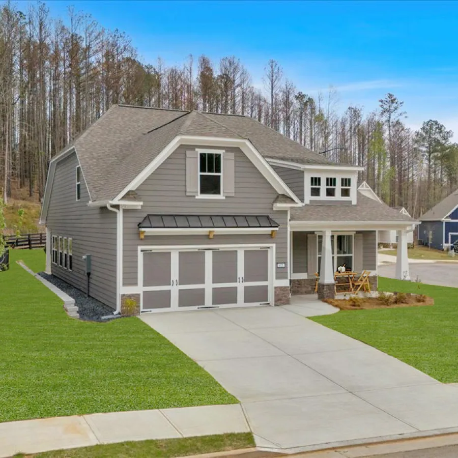 A picturesque gray house with a large yard surrounded by trees, showcasing a sunny neighborhood setting.