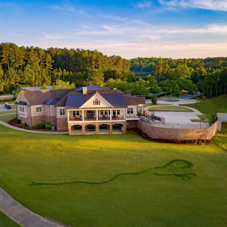 Large house with wraparound porch overlooking a green lawn with heart-shaped grass design at sunset.
