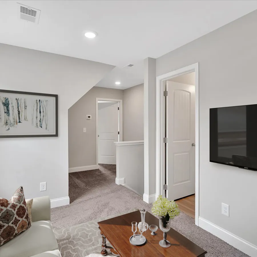 Modern living room with gray carpet, wall-mounted TV, wooden coffee table, light gray walls, and beige couch with pillows.