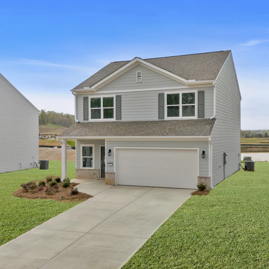 Two-story white suburban house with a double garage, concrete driveway, and green lawn under a blue sky.