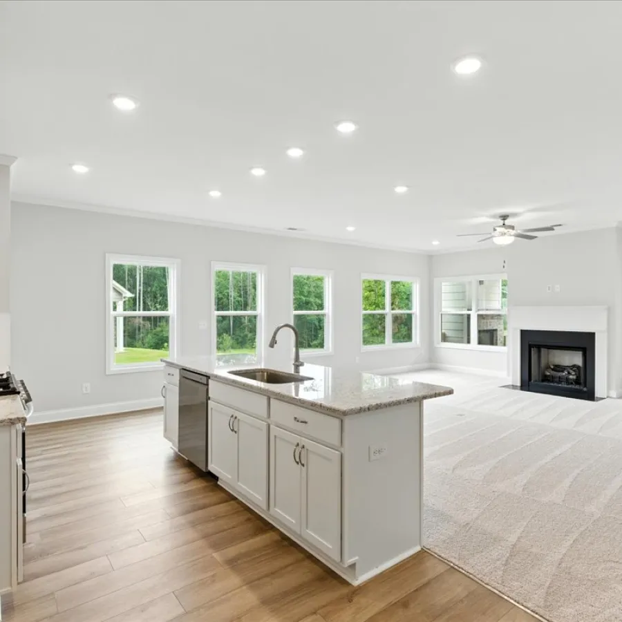 Bright open-concept kitchen and living room with white cabinetry, hardwood floors, fireplace, and large windows.