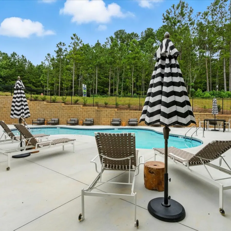 Outdoor pool area with lounge chairs and black-and-white striped umbrellas under a blue sky.