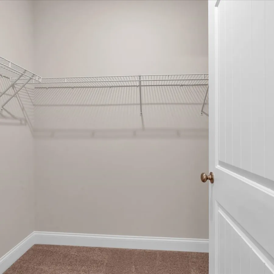 Empty walk-in closet with beige walls, carpeted floor, white wire shelves, and a partially open white door.