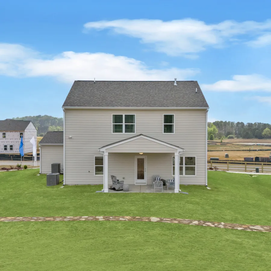 Rear view of a modern house with green lawn and clear blue sky, showcasing outdoor living space.