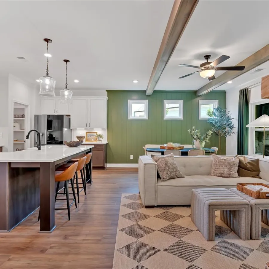Open concept kitchen and living room with white cabinets, dark island, green accent wall, and cozy seating area.