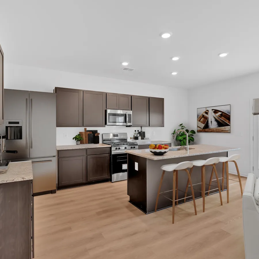 Modern kitchen with dark cabinets, stainless steel appliances, large island with stools, and light wood floors.