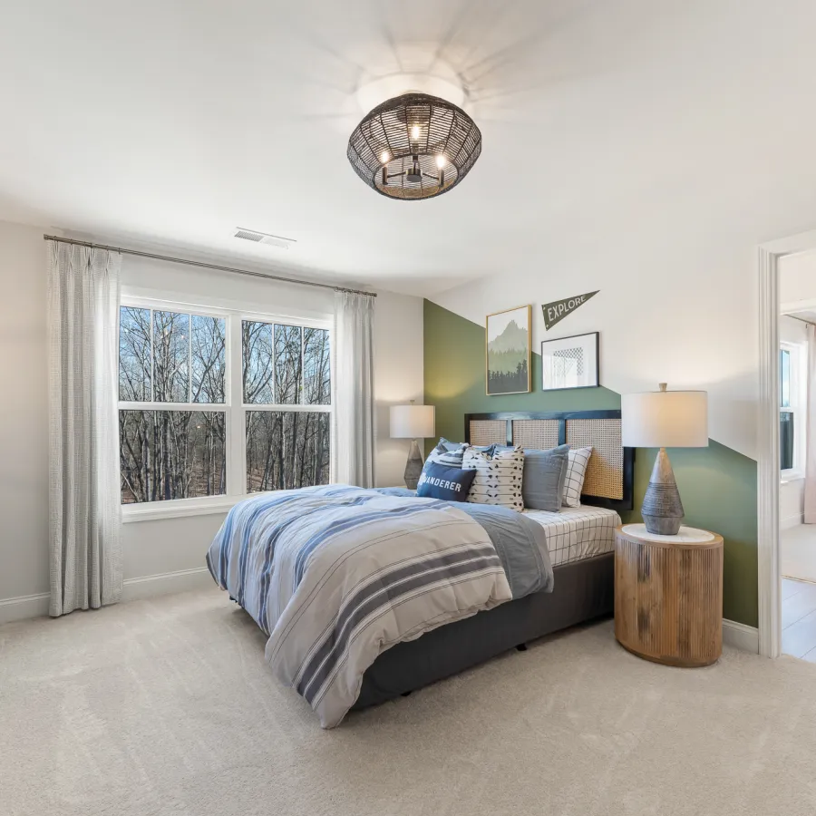 Bright modern bedroom with large window, gray bed and striped bedding, bedside lamps, and green accent wall.